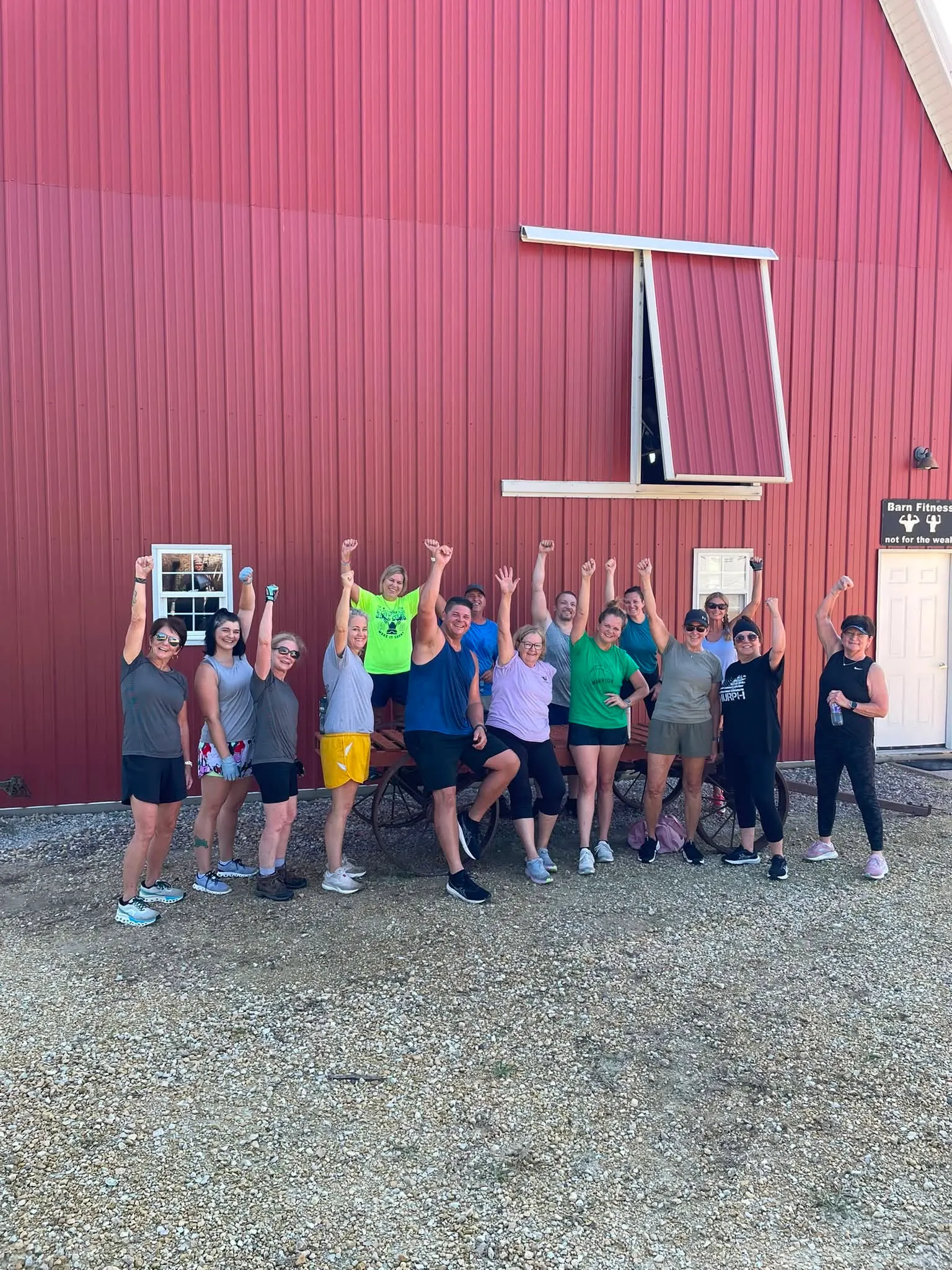 Barn Fitness members cheering with their arms raised in front of the red barn